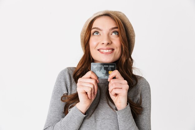 Retrato de uma mulher europeia dos anos 30 usando chapéu, sorrindo e segurando um cartão de crédito isolado no branco