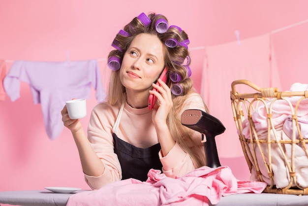 Retrato de uma mulher falando ao telefone enquanto toma café contra um fundo rosa