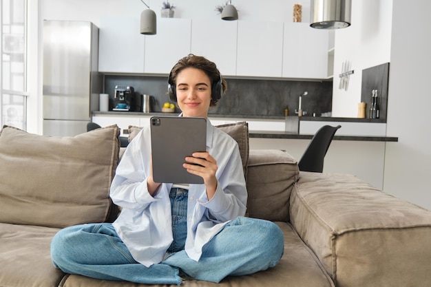 Retrato de uma mulher feliz assistindo vídeo em tablet em fones de ouvido trabalhando em casa usando seu digital d