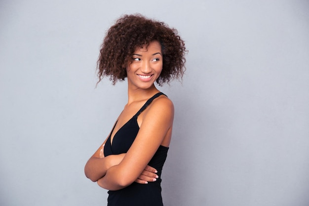 Retrato de uma mulher feliz com os braços cruzados em pé sobre uma parede cinza e olhando para longe