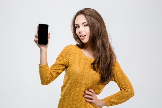 Retrato de uma mulher feliz e casual mostrando a tela do smartphone em branco, isolada em um fundo branco