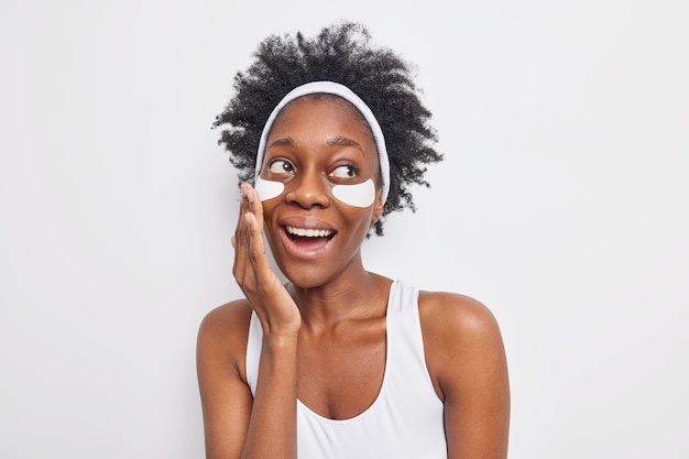 Retrato de uma mulher feliz e despreocupada de pele escura com cabelo cacheado natural que aplica manchas de beleza para reduzir amplamente o sorriso