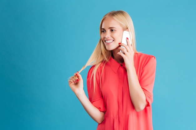 Retrato de uma mulher feliz falando ao telefone e olhando para longe, por cima de uma parede azul