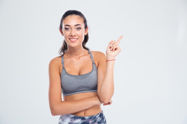 Retrato de uma mulher feliz fitness apontando o dedo isolado em uma parede branca