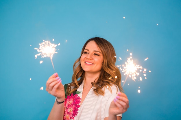 Retrato de uma mulher feliz segurando luzes de Bengala sobre fundo azul com espaço de cópia. Conceito de Natal, celebrações e feriados