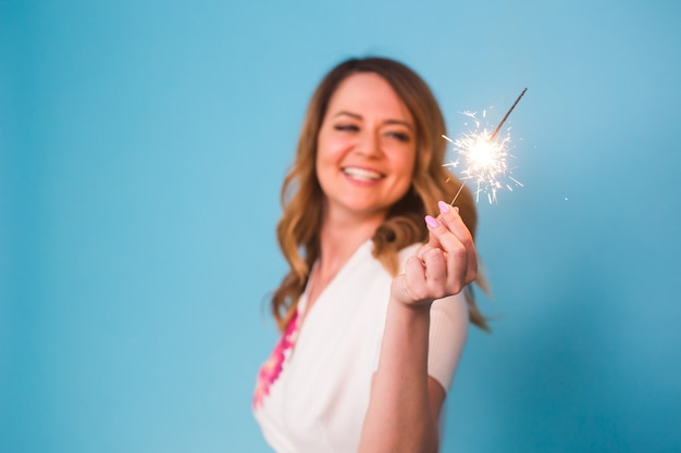 Retrato de uma mulher feliz segurando luzes de Bengala sobre fundo azul com espaço de cópia. Conceito de Natal, celebrações e feriados