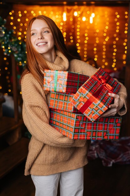 Retrato de uma mulher feliz segurando muitas belas caixas de presentes de Natal no fundo das luzes de Natal