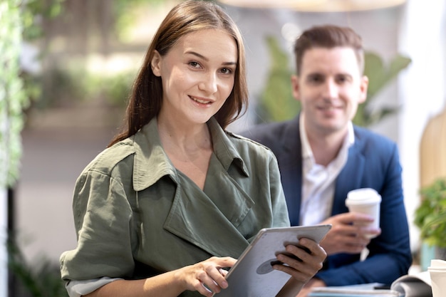 Retrato de uma mulher feliz segurando o dispositivo tablet e sentado no bar do balcão de café com pessoas colegas no fundo hora do café de negócios de conceito com trabalho de tecnologia inteligente