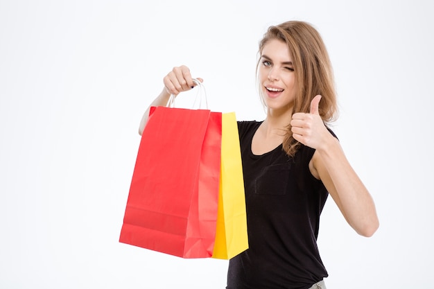 Retrato de uma mulher feliz segurando sacolas de compras e aparecendo o polegar isolado em um fundo branco