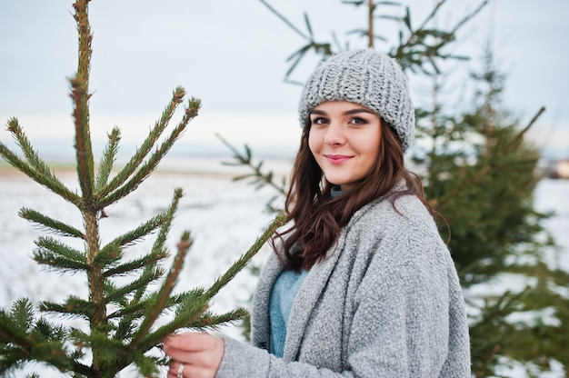 Retrato de uma mulher gentil no casaco cinza e chapéu contra a árvore de natal ao ar livre.