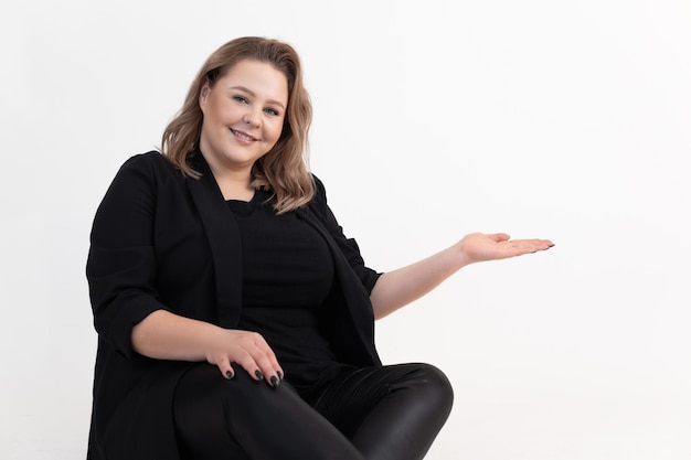 Retrato de uma mulher gorda gorda de meia-idade sorridente em leggings de cardigan preto sentado e segurando a mão w