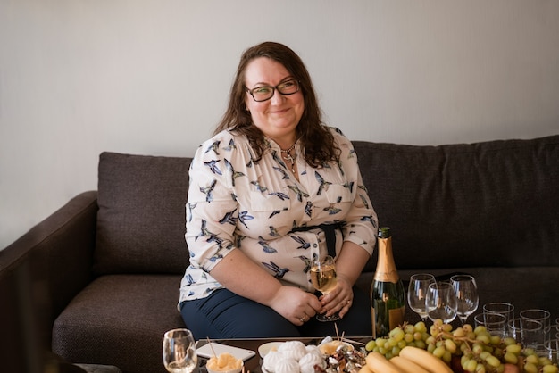 Foto retrato de uma mulher grande de óculos com uma taça de vinho, sentada no sofá