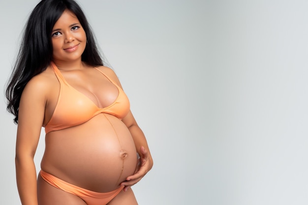 Retrato de uma mulher grávida com cabelos pretos em um sutiã laranja em um fundo branco