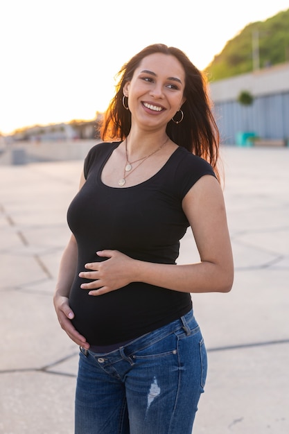 Retrato de uma mulher grávida hispânica caminhando no aterro ao pôr do sol no conceito de gravidez e maternidade