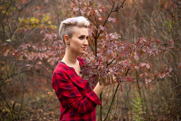 Retrato de uma mulher hipster estilosa com corte de cabelo curto no fundo do outono com árvores de outono murchas
