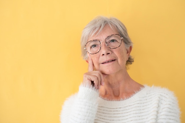 Retrato de uma mulher idosa atraente usando óculos com uma expressão pensativa, fundo amarelo