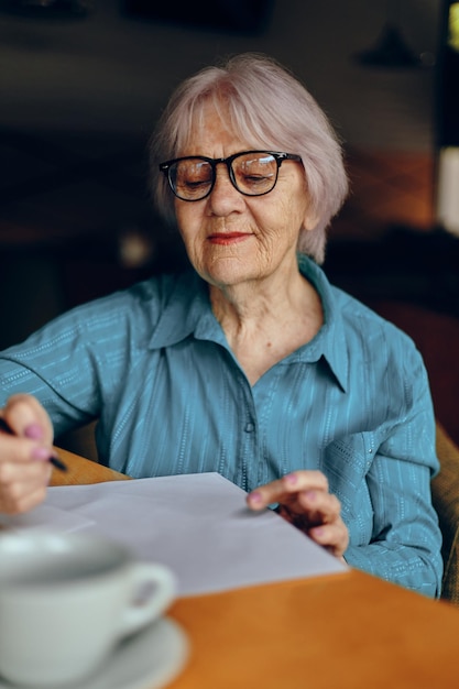 Retrato de uma mulher idosa com óculos se senta em uma mesa em frente a um estilo de vida de laptop inalterado