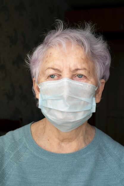 Foto retrato de uma mulher idosa com uma máscara médica no rosto. um pensionista de suéter azul com olhos azuis doentes.