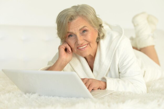 Retrato de uma mulher idosa deitada na cama com um laptop