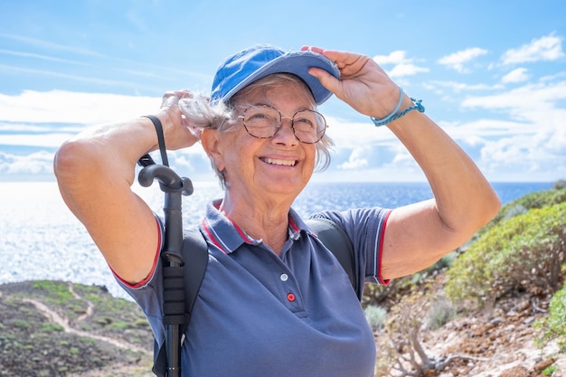 Retrato de uma mulher idosa feliz caminhando em um dia de caminhada em uma trilha ao ar livre em uma excursão entre o mar e o campo Mulher caucasiana relaxada desfrutando de aventura ou aposentadoria levando um estilo de vida saudável