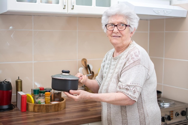 Retrato de uma mulher idosa segurando uma panela de cozinha na cozinha