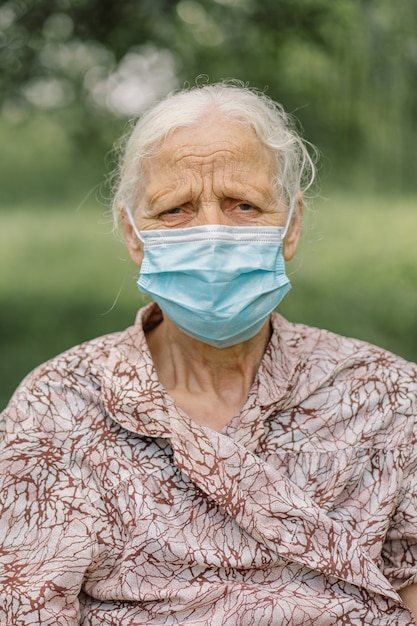 Retrato de uma mulher idosa triste de cabelos grisalhos sozinha usando máscara protetora durante a quarentena de covid-19.