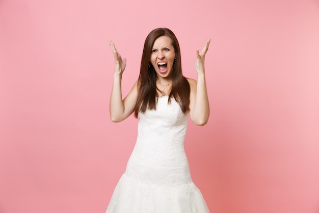 Retrato de uma mulher irritada com raiva em um lindo vestido branco em pé gritando, espalhando as mãos