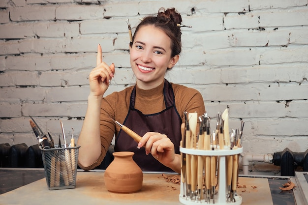 Foto retrato de uma mulher jovem e alegre, segurando um vaso de barro. o oleiro faz um vaso à mesa de uma olaria. conceito de inspiração e ideias