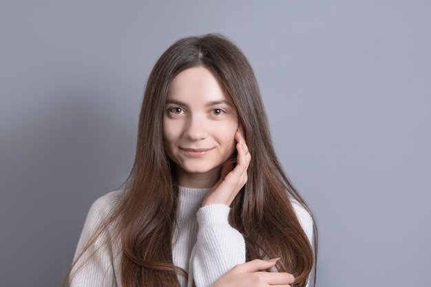 Retrato de uma mulher jovem e atraente com cabelo comprido escuro, sorrindo facilmente em um fundo cinza do estúdio. Lugar para texto. Com espaço de cópia.