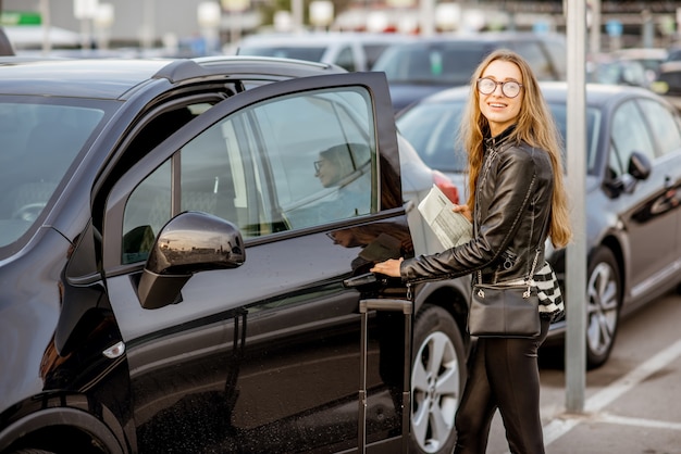 Retrato de uma mulher jovem e feliz abrindo a porta do carro alugado ao ar livre no estacionamento