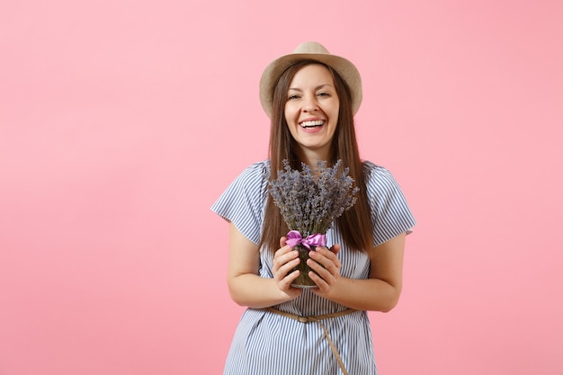 Retrato de uma mulher jovem e feliz concurso em vestido azul, chapéu segurando o buquê de flores de lavanda roxas lindas isoladas em um fundo rosa tendência brilhante. Conceito de feriado do dia internacional da mulher.