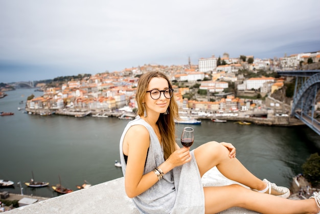 Retrato de uma mulher jovem e feliz, saboreando o vinho do Porto, sentado no terraço com uma bela vista da cidade do Porto, Portugal