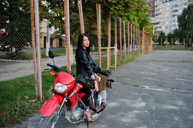 Retrato de uma mulher legal e incrível de vestido e jaqueta de couro preta sentada em uma moto vermelha legal