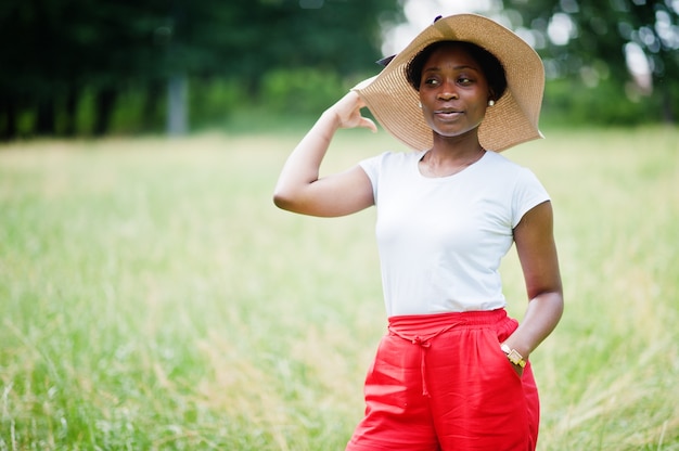 Retrato de uma mulher linda com chapéu de verão, calça vermelha e camiseta branca, posando no parque