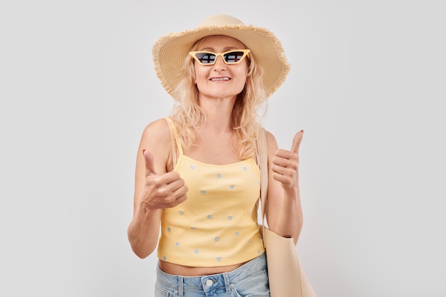 Retrato de uma mulher madura em roupas de verão sorrindo alegremente mostrando polegares para cima gesto isolado no fundo branco do estúdio aprova boa escolha decisão certa