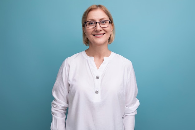 Retrato de uma mulher madura sorridente com cabelos loiros usando óculos e uma camisa branca