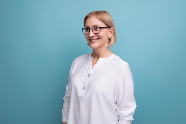 Retrato de uma mulher madura sorridente e saudável com cabelos loiros em óculos e uma blusa branca em um azul