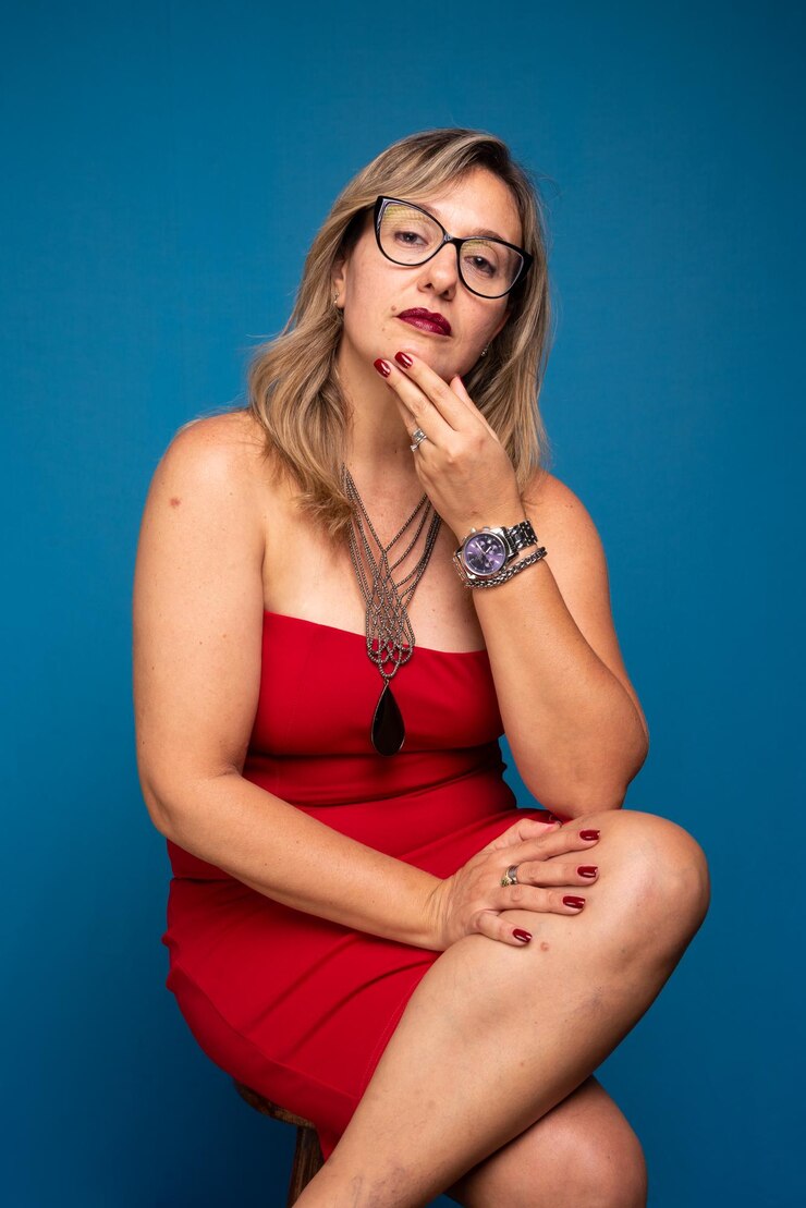 Foto retrato de uma mulher madura vestindo roupa vermelha sentada com as mãos no queixo pessoa positiva e confiante isolada em fundo azul