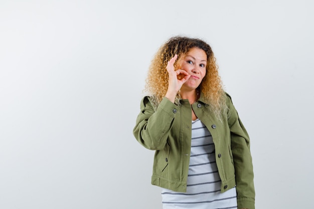 Foto retrato de uma mulher maravilhosa mostrando gesto de zíper em jaqueta verde, camisa e olhando a vista frontal cuidadosa