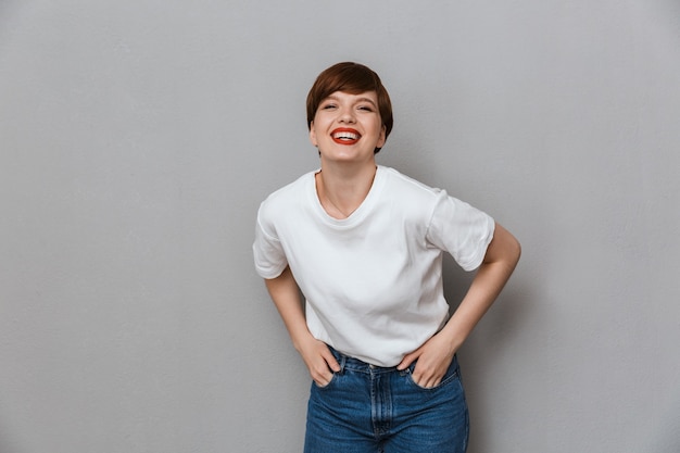 Retrato de uma mulher morena alegre vestindo uma camiseta casual sorrindo na frente isolada sobre uma parede cinza