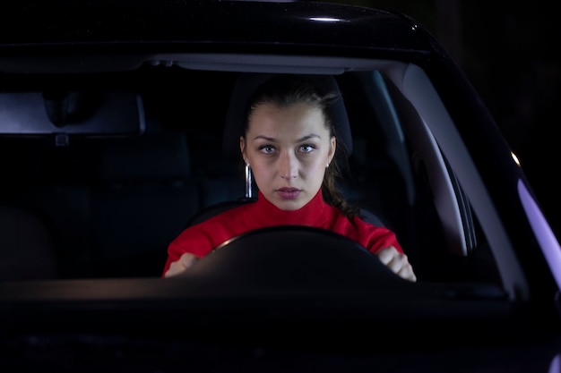 Retrato de uma mulher morena de cabelos compridos com uma camisola vermelha num carro a conduzir à noite