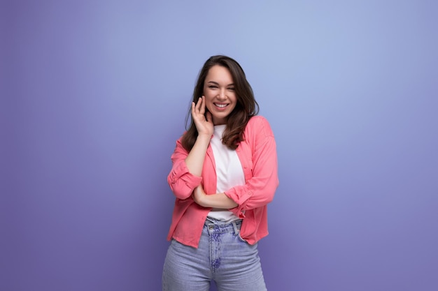 Retrato de uma mulher morena em uma camisa e jeans posando com um sorriso em um fundo de estúdio