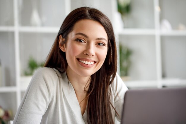 Retrato de uma mulher morena trabalhando em um escritório com um laptop Uma mulher com um laptop olha para a câmera e sorri docemente