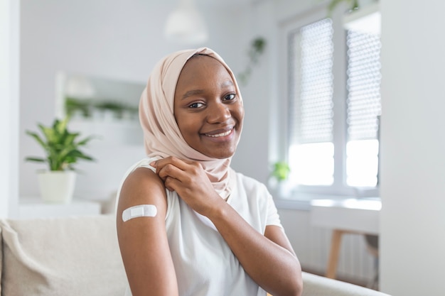 Retrato de uma mulher muçulmana africana sorrindo depois de tomar a vacina. Mulher segurando a manga da camisa e mostrando o braço com curativo após receber a vacinação.