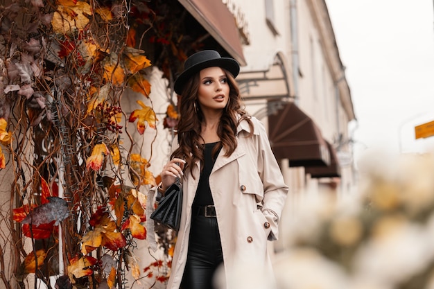 Retrato de uma mulher muito elegante com um chapéu estiloso em um casaco cinza da moda e uma bolsa de mão andando pela cidade com folhagem amarela de outono