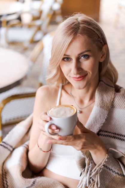 Retrato de uma mulher muito loira sorrindo em uma manta aconchegante sentada no café