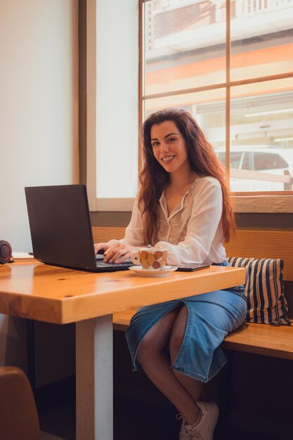 Retrato de uma mulher olhando para a câmera enquanto ela está trabalhando com seu laptop