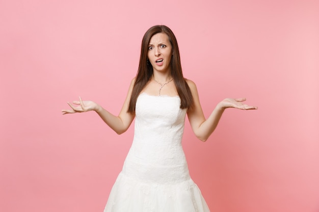 Retrato de uma mulher preocupada e preocupada em um elegante vestido de renda branca em pé e estendendo as mãos