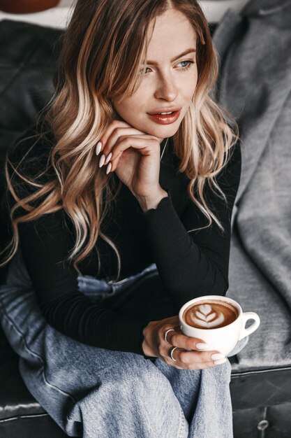 Retrato de uma mulher, que está sentada em um sofá e ela está segurando uma xícara de café.