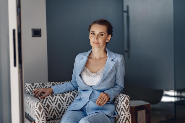 Retrato de uma mulher respeitada séria formal vestindo um terno formal azul e posando enquanto está sentado em uma poltrona. Conceito de trabalho